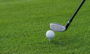 Golf club poised to hit a golf ball on a tee, set against a lush green grass background.