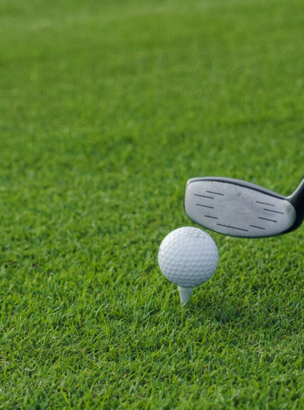 Golf club poised to hit a golf ball on a tee, set against a lush green grass background.
