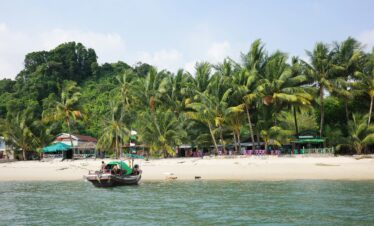 A serene beach with palm trees and traditional boat in Myeik, Myanmar.