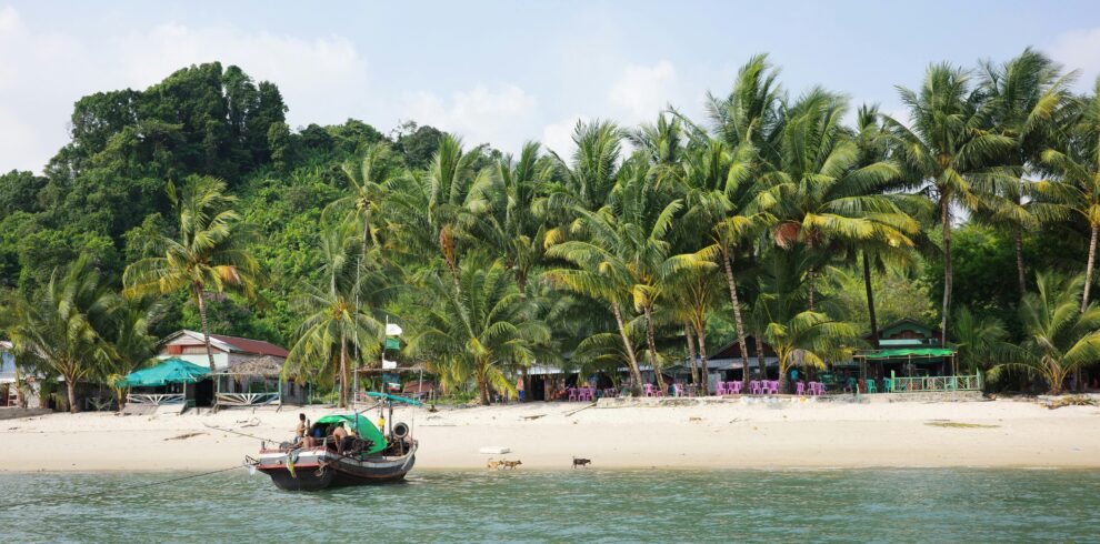 A serene beach with palm trees and traditional boat in Myeik, Myanmar.