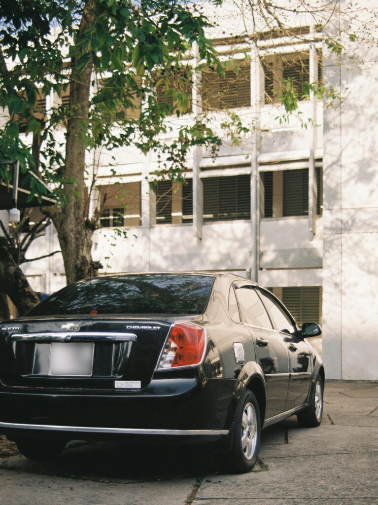 A black Chevrolet parked near a multi-story urban building surrounded by trees.